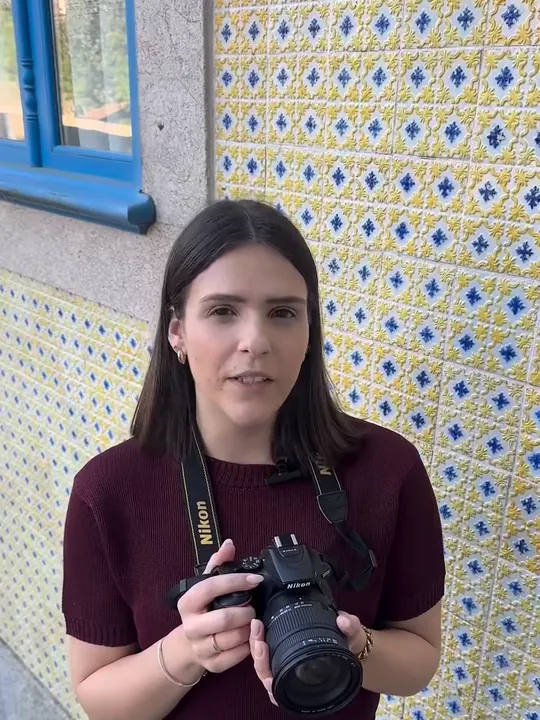 Gabriela Noivo com uma câmara fotográfica, em frente a uma parede de azulejos